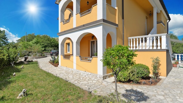 A two-story building with a yellow facade, white arches, and a stone pathway leading to the entrance.
