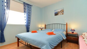 A bedroom with a bed, two bedside tables, a window with blue curtains, and a painting on the wall.