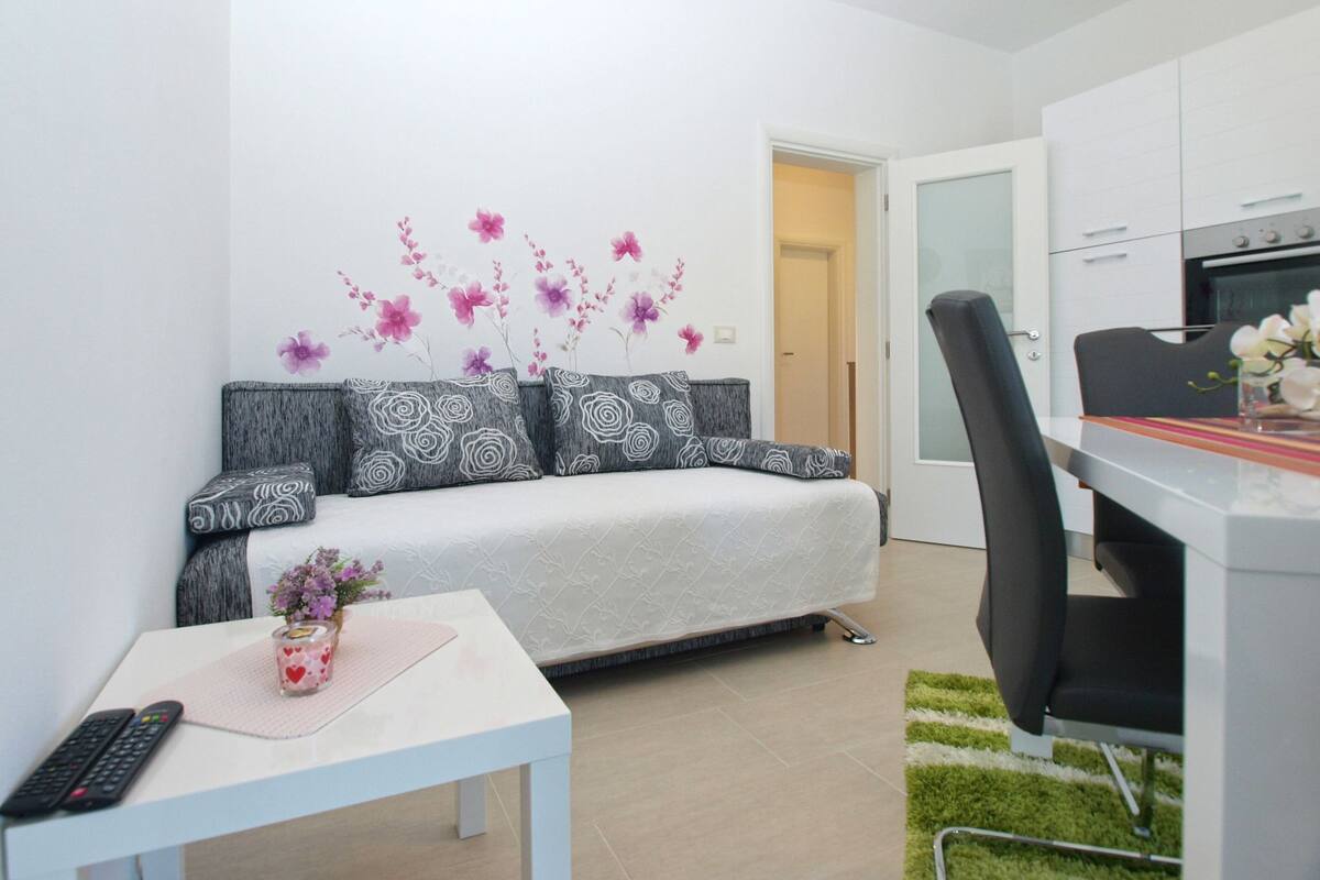 A modern living room with a sofa, a small table, a remote control, and a vase with flowers.