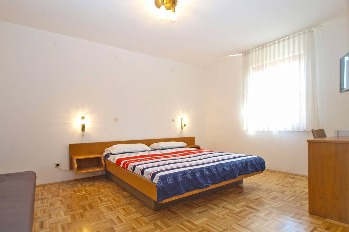 A bedroom with a wooden bed, two bedside lamps, a wooden desk, and a window with curtains.