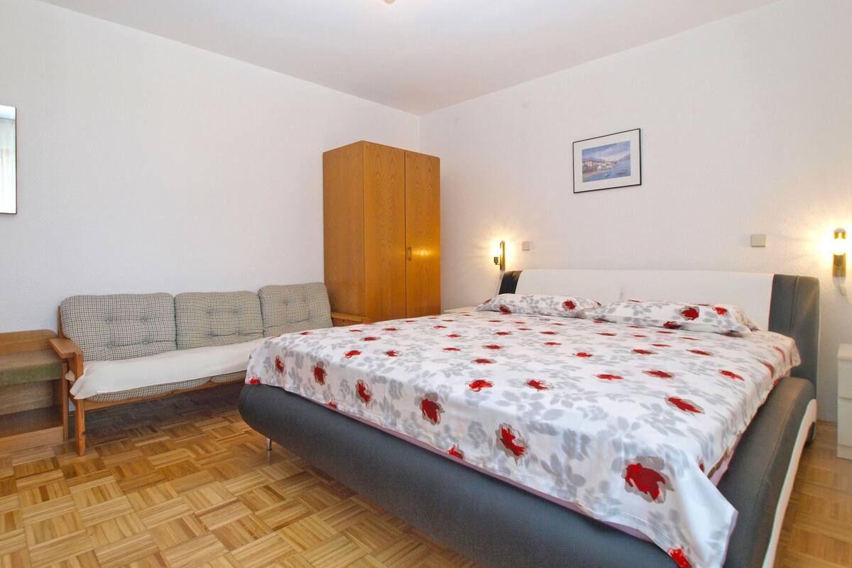 A bedroom with a bed, a wooden wardrobe, a sofa, and a wall-mounted light fixture.