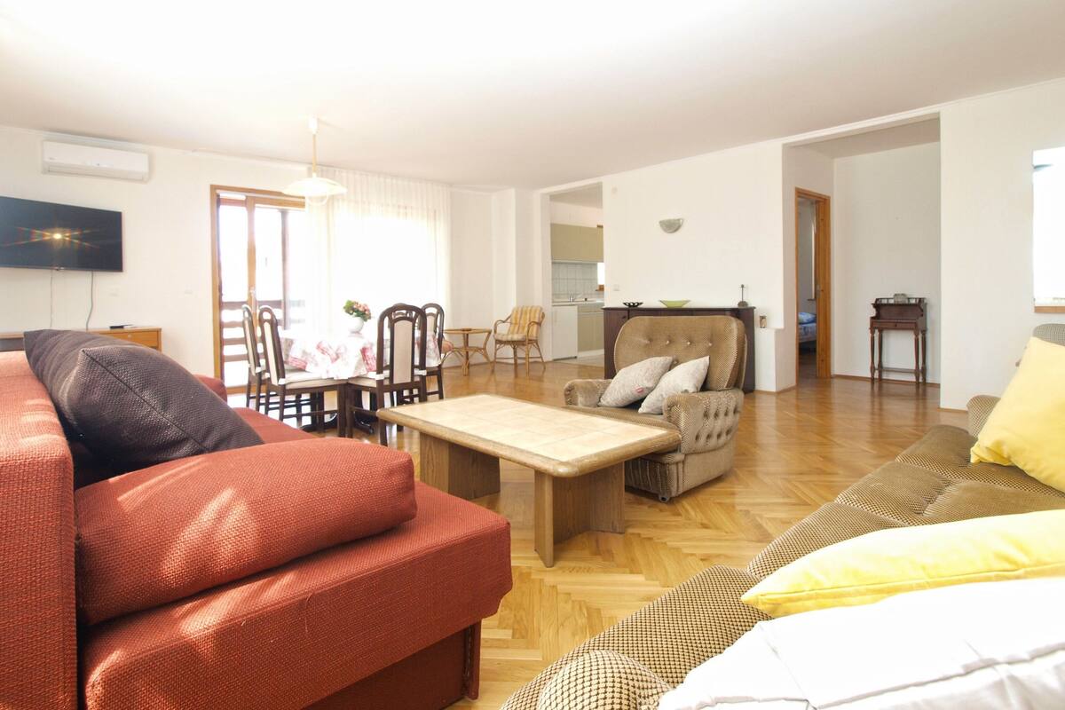 A spacious living room with a sofa, armchair, and a dining area with chairs and a table.