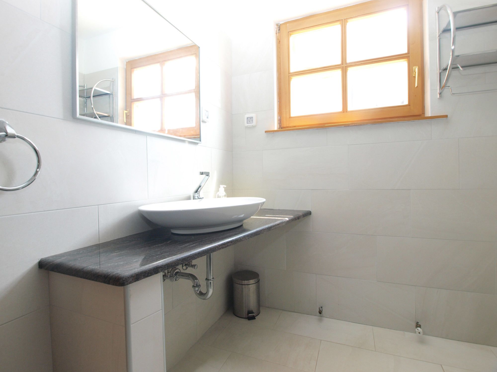 A bathroom with a white sink, a mirror, a window, and a trash can.