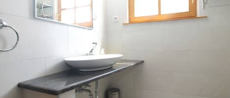 A bathroom with a white sink, a mirror, a window, and a trash can.