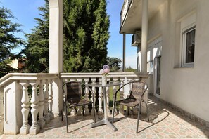 Ein Balkon mit zwei Korbstühlen, einem kleinen runden Tisch, einem weißen Geländer und einer Vase mit Blumen.