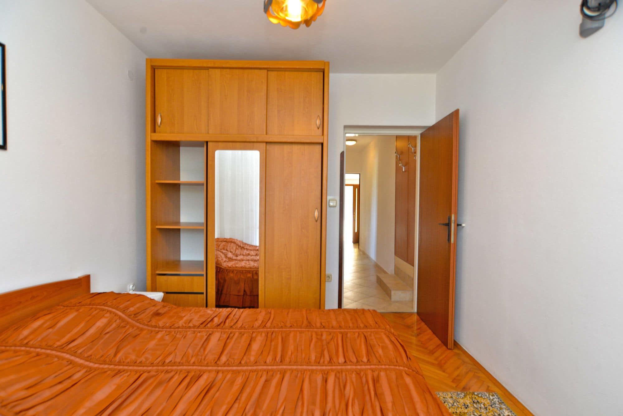 A bedroom with a bed, wooden wardrobe, and a door leading to another room.