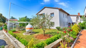 A two-story building with a white facade and brown roof, surrounded by a well-maintained garden with various plants and flowers. - Apartment 1633 (Pula)