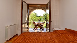 A room with a bed, a window, and an open door leading to a balcony with a table and chairs. - Apartment 1633 (Pula)