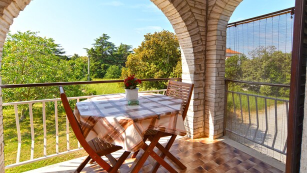 A covered patio with a table and chairs, stone arches, and a view of greenery. - Apartment 1633 (Pula)
