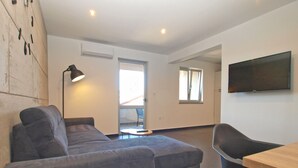 Una sala de estar moderna con un sofá gris, una mesita redonda y un televisor montado en la pared.