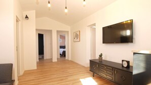 Una sala moderna con piso de madera, un sofá gris, un sillón verde azulado, un mueble negro para televisión y un televisor montado en la pared.