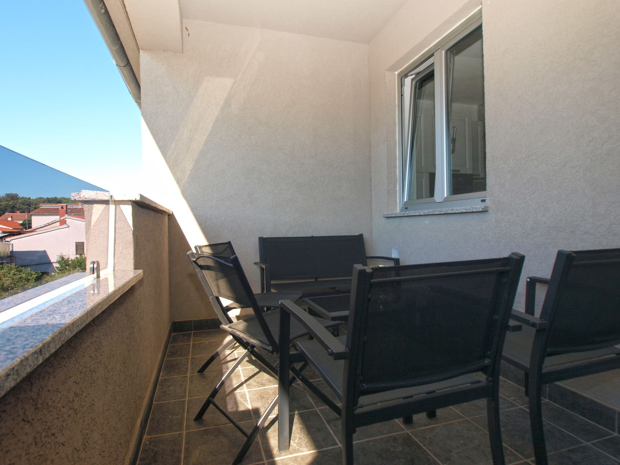 Un balcón con mesa y sillas, una ventana y vistas a edificios.