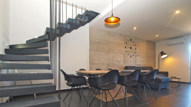 Un interior moderno con una escalera, comedor y un reloj en la pared.