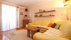 A living room with a yellow sofa, a wooden coffee table, and a bookshelf with books and decorative items. - Apartment 1635 (Pula)