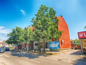 Stylish red-brick building with a flat roof, surrounded by lush greenery and parked vehicles.
