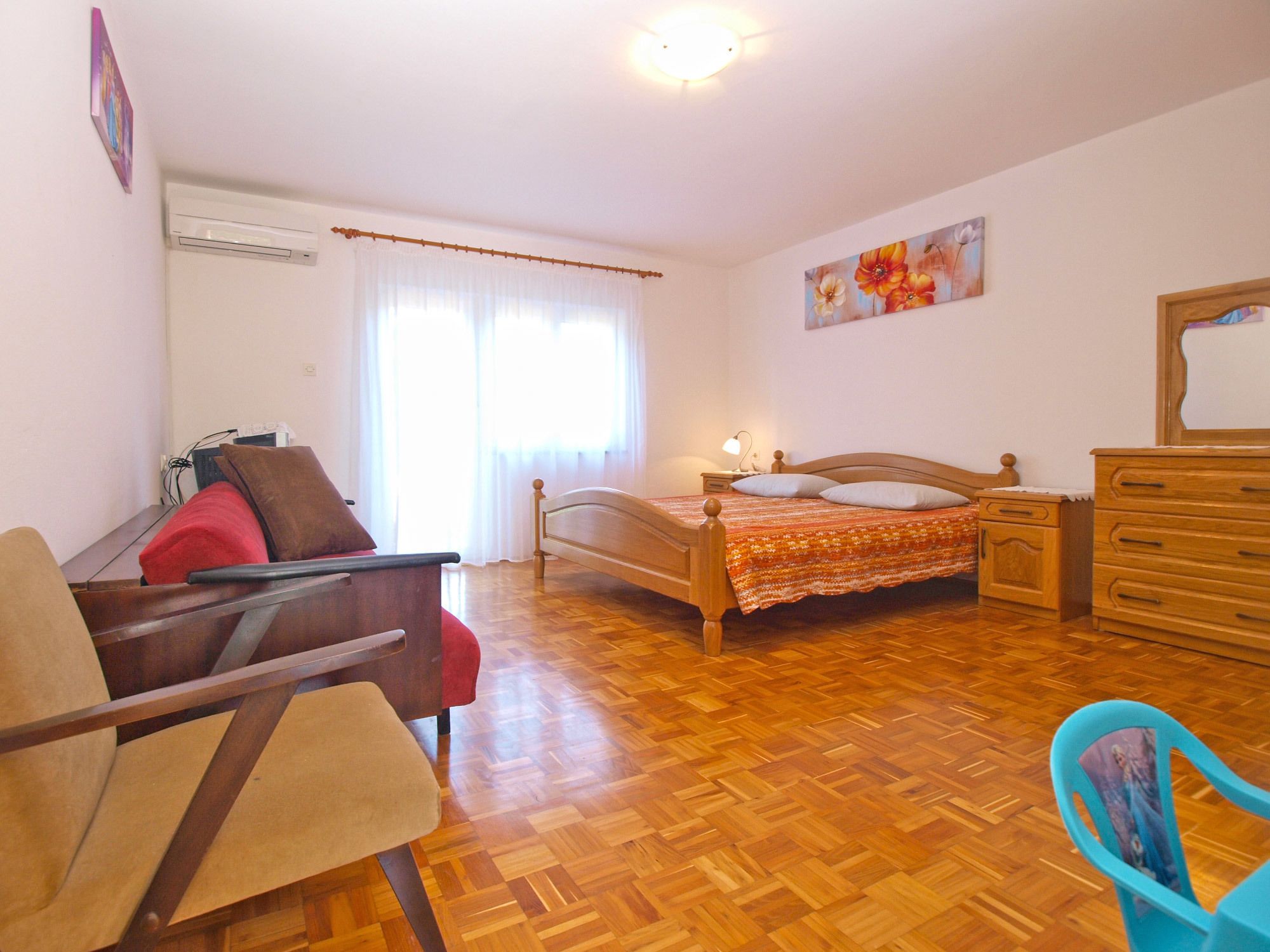 Ein Schlafzimmer mit einem hölzernen Bett, einem Sessel, einer Kommode und einem Nachttisch.