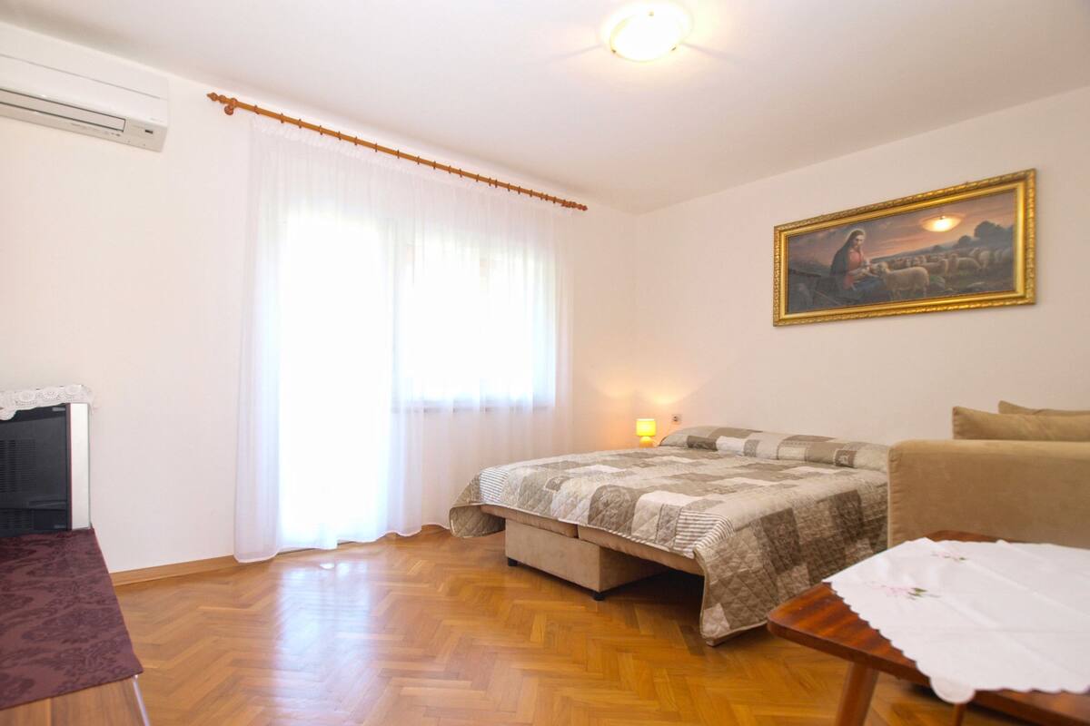 Quarto com cama, mesa de cabeceira, cadeira e um quadro na parede.