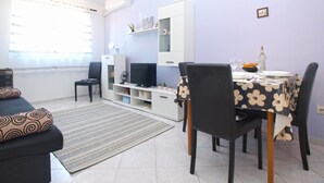 A modern living room with a dining area, featuring a sofa, a TV, a dining table with chairs, and a small kitchen area. - Apartment 1639 (Pula)