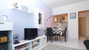 A modern living room with a flat-screen TV, a white entertainment unit, and a dining area with a floral tablecloth. - Apartment 1639 (Pula)