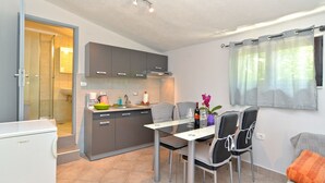 A compact kitchen with grey cabinets, a dining table with four chairs, and a window with curtains. - Apartment 1642 (Pula)
