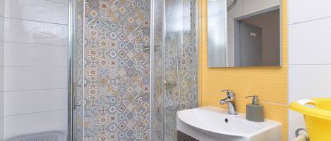 Un baño con ducha, lavamanos y espejo.