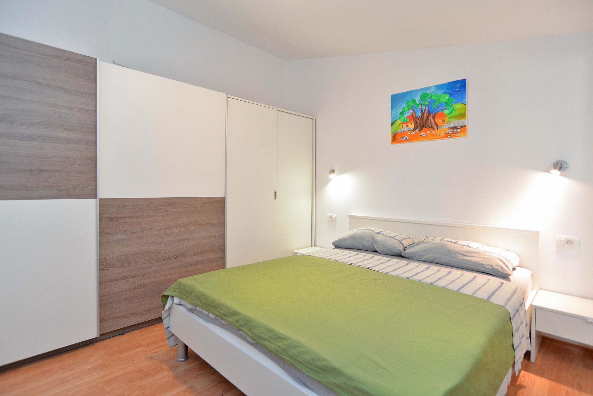Ein Schlafzimmer mit Bett, Kleiderschrank, Nachttisch und einem Bild an der Wand.