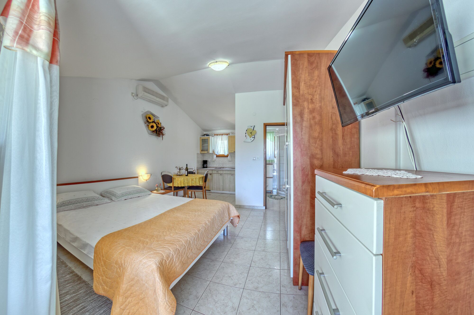 Ein Schlafzimmer mit einem Bett, einem Schreibtisch, einem Fernseher und einem angrenzenden Badezimmer.