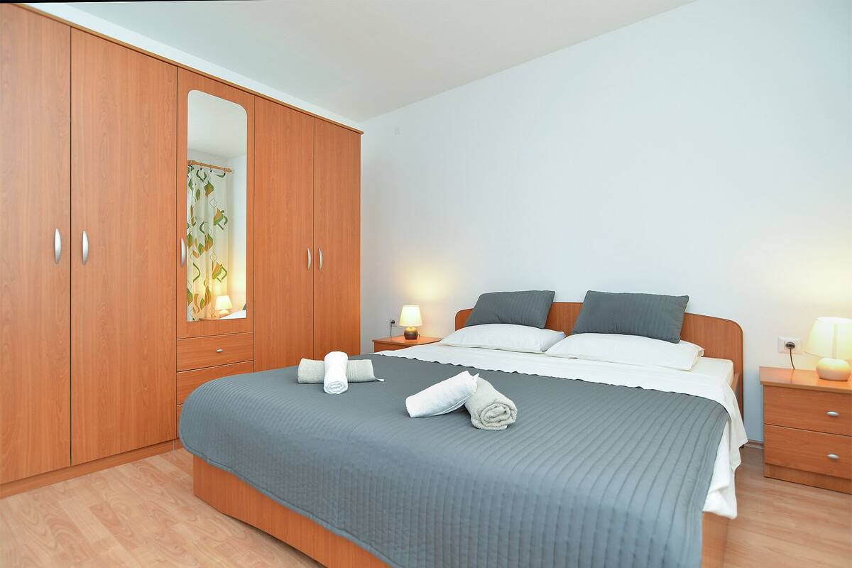 A bedroom with a large wardrobe, a bed with a grey bedspread, two bedside tables with lamps, and a mirror in the wardrobe.
