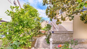 Un sentier de jardin mène à un escalier en pierre doté d’une balustrade blanche, le tout étant entouré d’une végétation luxuriante et de plantes en fleurs.