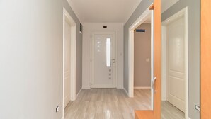 Un couloir avec une porte au fond, un interrupteur sur le mur et un banc en bois dans un coin.
