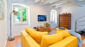 A bright living room with a yellow sofa, a wooden dresser, and a television on the wall. - House 1650 (Vodnjan)