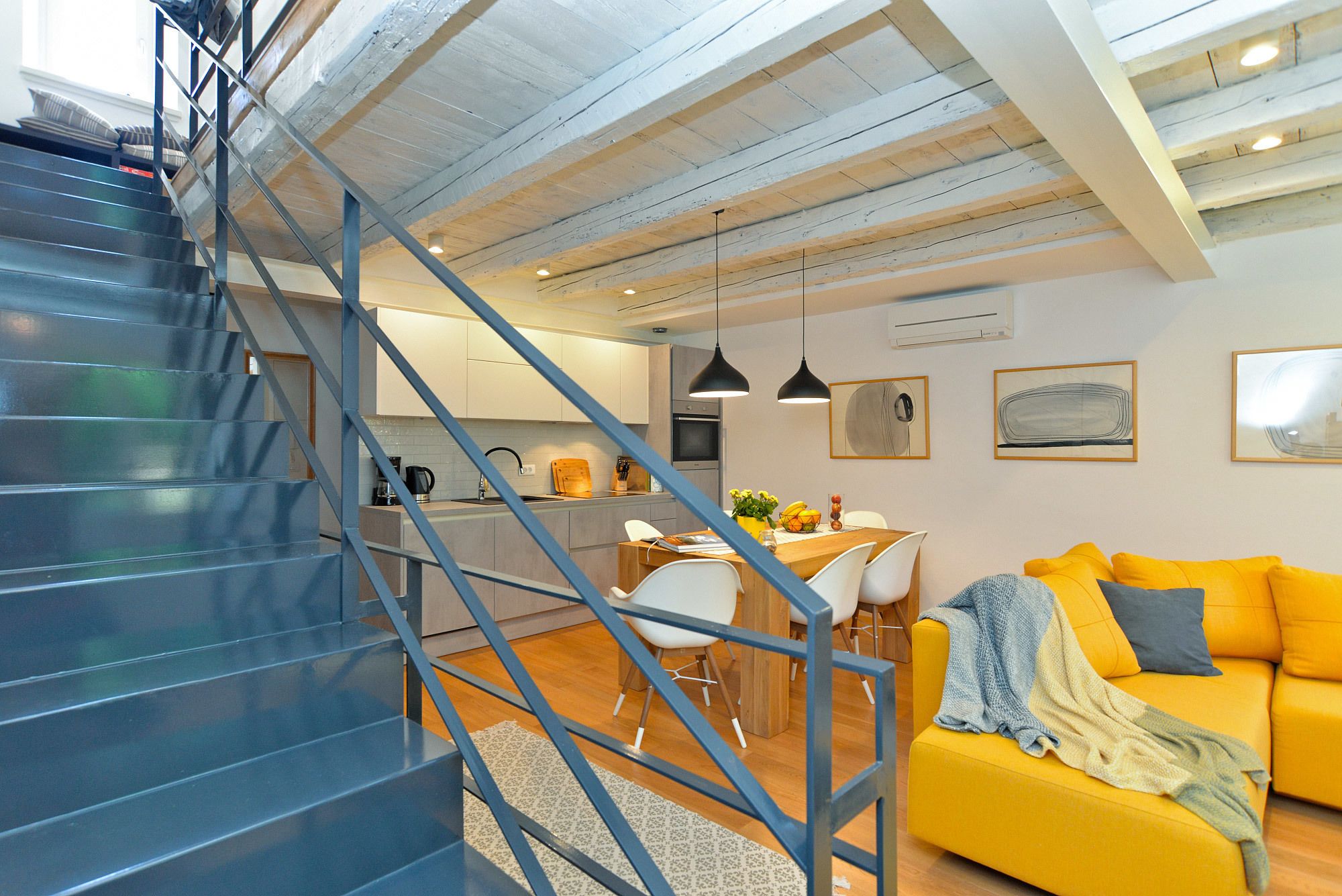 Um interior moderno com escada, área de refeições e sala de estar com sofá amarelo.