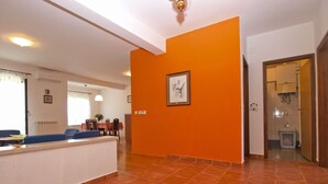 Un'ampia zona giorno con pavimento piastrellato, una sala da pranzo con tavolo e sedie, e una cucina visibile attraverso un'apertura.