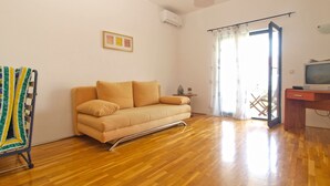 Un soggiorno con un divano, una televisione su un mobile in legno, un tavolino con una pianta e una finestra con tende.