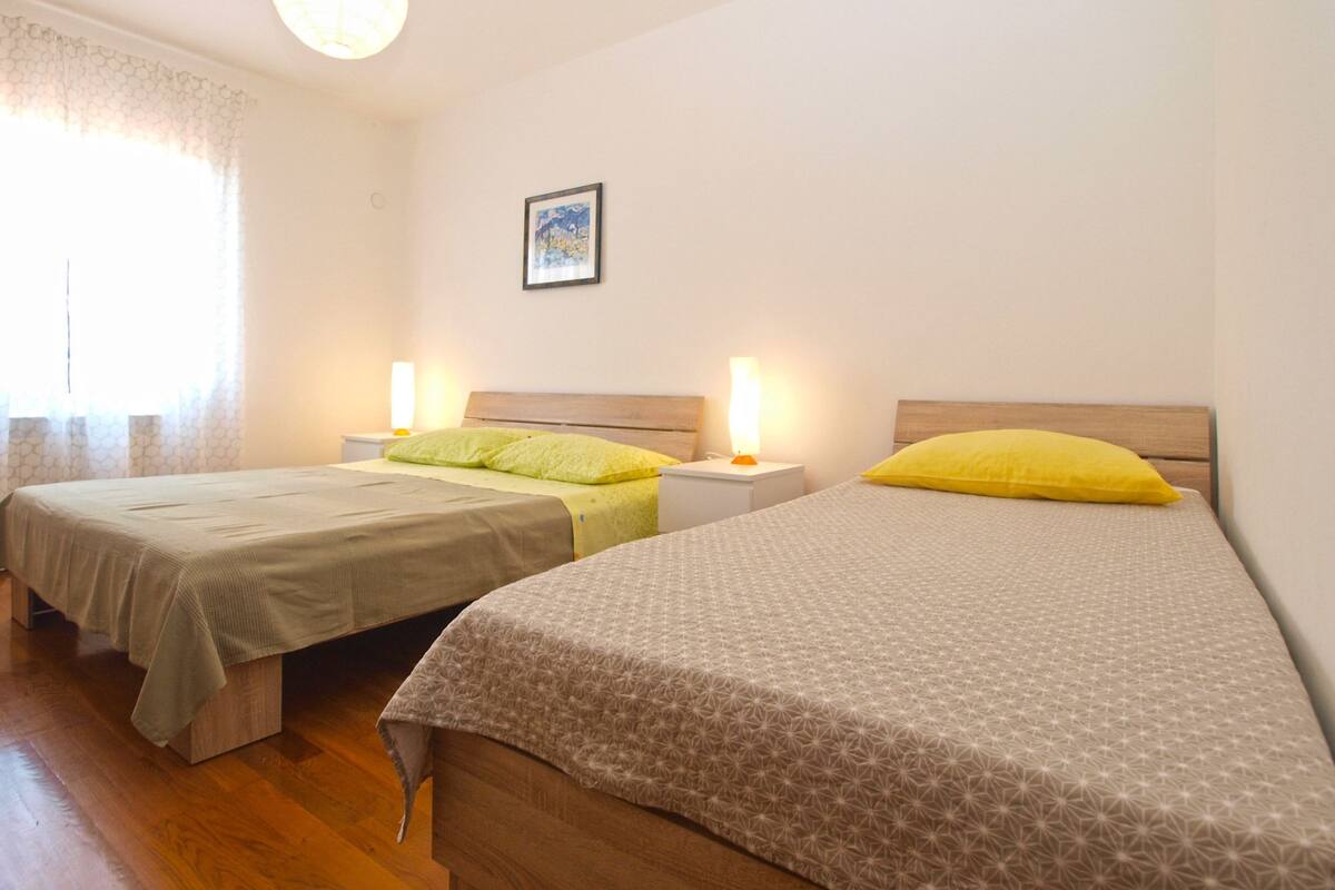 Deux lits simples avec des têtes de lit en bois, des tables de chevet avec des lampes et un tableau encadré au mur.