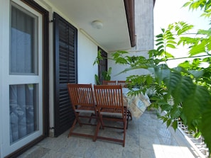 A balcony with two wooden chairs and a table, surrounded by potted plants.