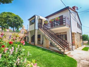 Una casa de dos pisos con fachada de piedra, un balcón con plantas en macetas y una escalera que conduce al piso superior.