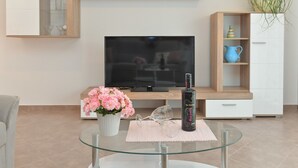 Een moderne woonkamer met een glazen salontafel, een televisie, een kast en een vaas met bloemen.