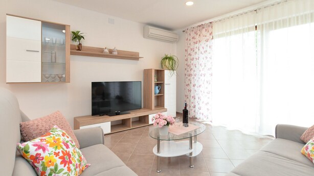 Een moderne woonkamer met een flatscreen televisie, een glazen salontafel, een bank en een kast met glazen deuren.