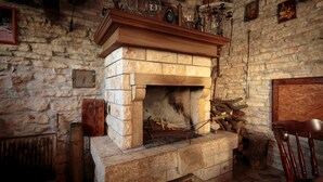 A stone fireplace with a wooden mantel, surrounded by stone walls and a rustic wooden chair. - Apartment 1655 (Kanfanar)