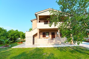 A two-story house with a stone facade, a balcony, and a well-maintained lawn.