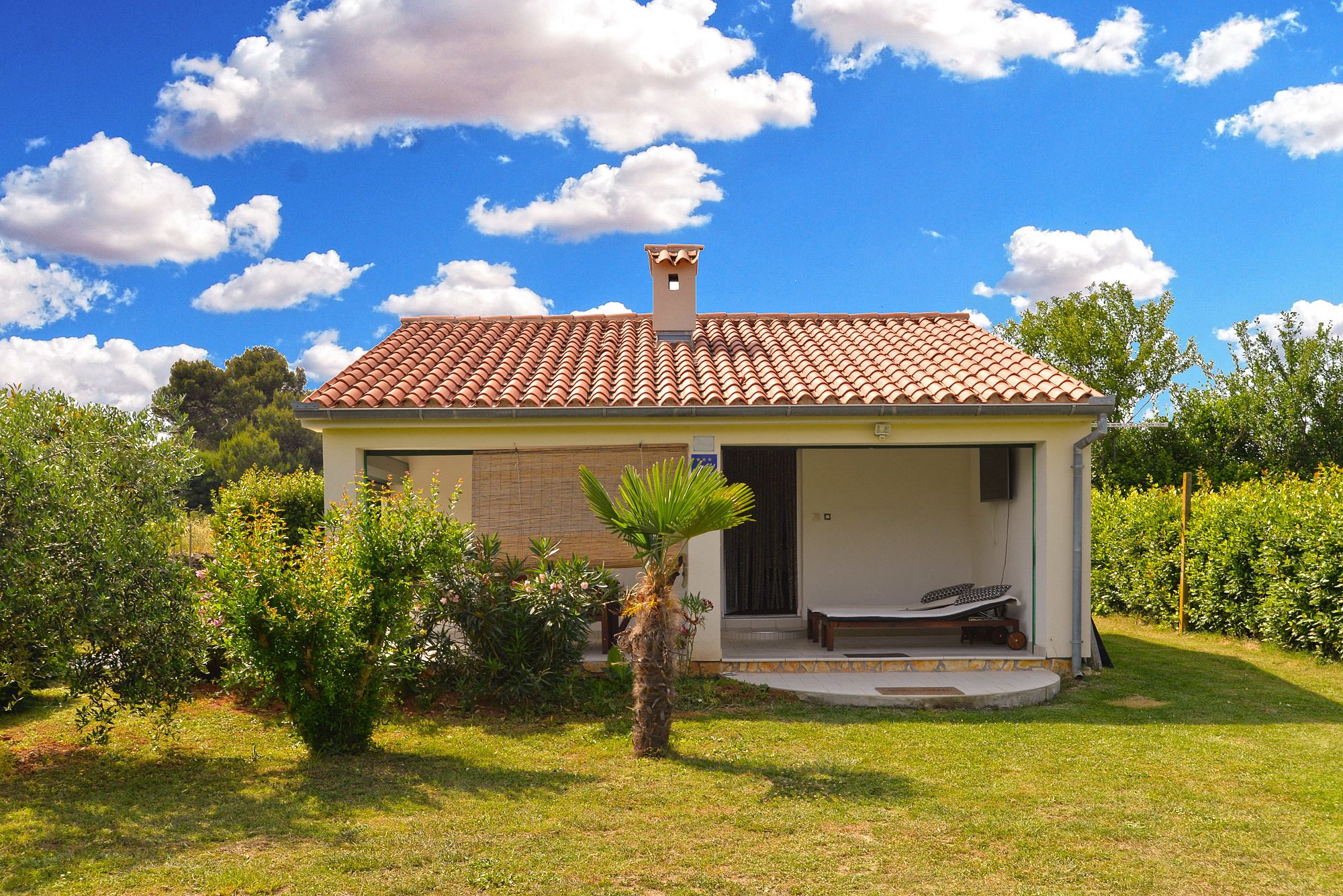 A small house with a tiled roof, a covered porch, and a garden in front.