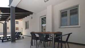 A modern outdoor patio with a wooden table and black chairs, surrounded by a tiled floor and a pergola structure. - Apartment 1670 (Fazana)