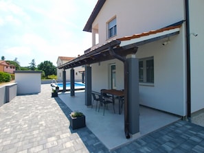 Ein überdachter Patio-Bereich mit Pool, Sitzgelegenheiten im Freien und Blick auf angrenzende Häuser.