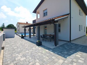 Ein modernes Haus mit überdachter Terrasse, Schwimmbad und Pflasterterrasse.