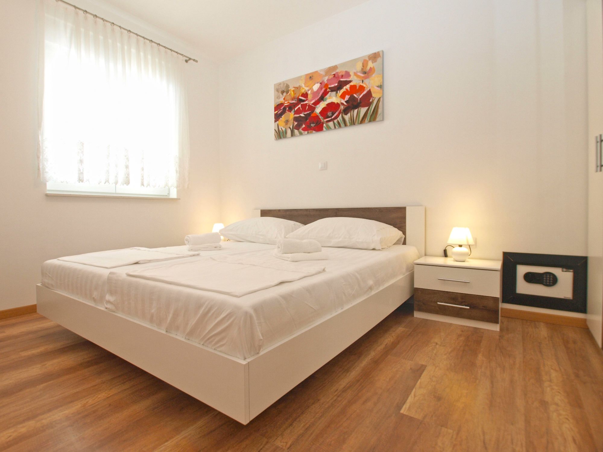 A neatly made bed with white linens, a bedside table with a lamp, and a framed picture on the wall.