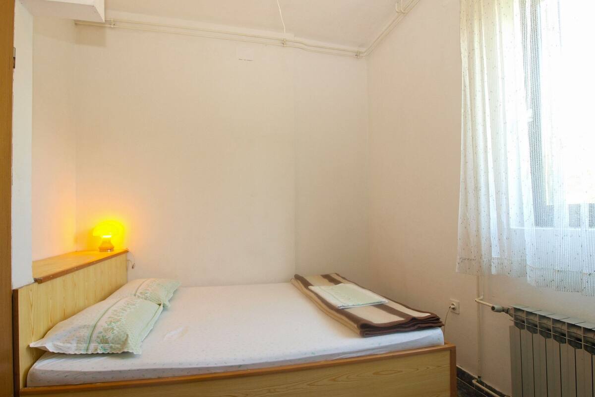 A small, single-bed room with a wooden headboard, a bedside lamp, and a radiator.