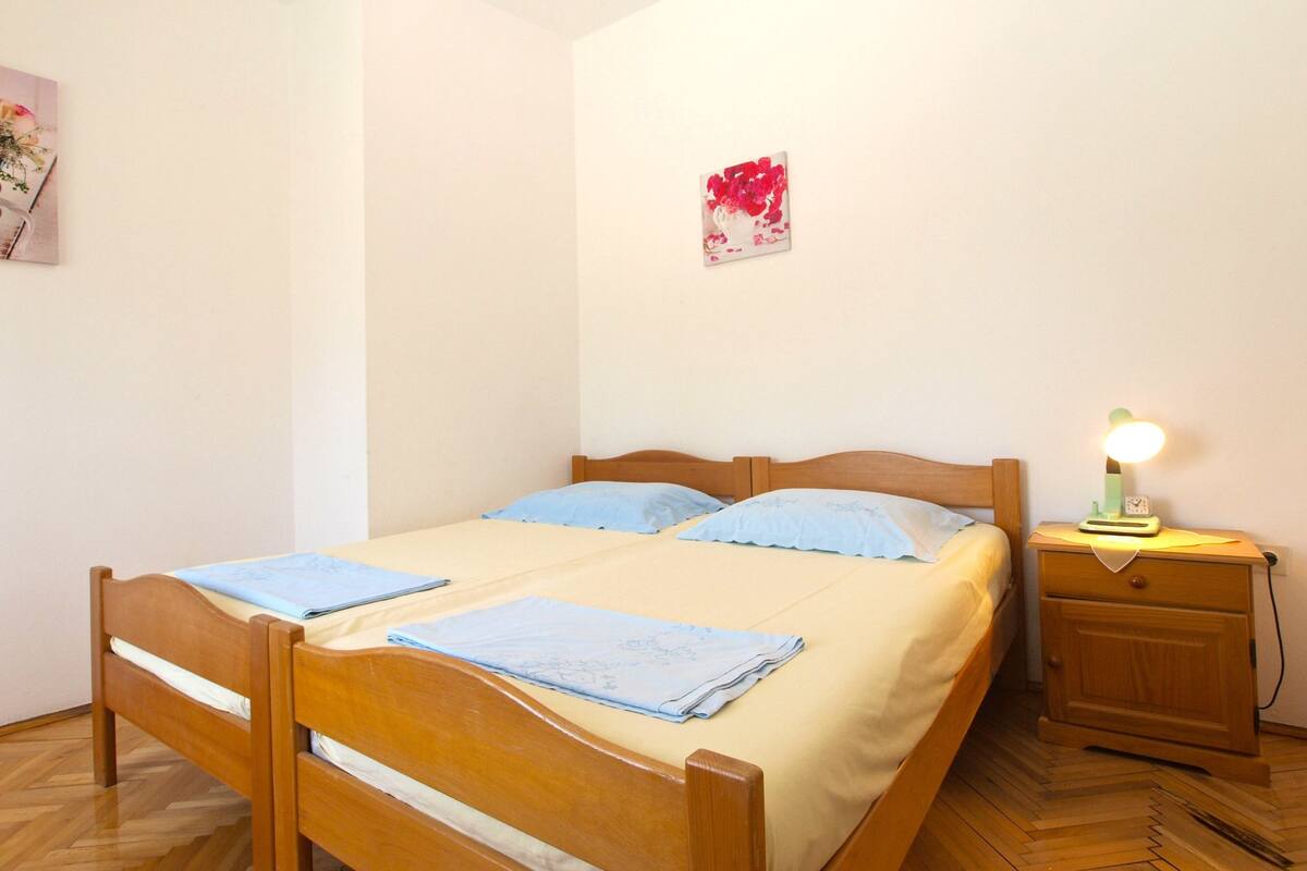 A single bed with a wooden frame, a nightstand with a lamp, and a wall-mounted picture.