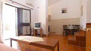 Une pièce comprenant un lit, un téléviseur posé sur un meuble, une table à manger avec des chaises et un coin cuisine.