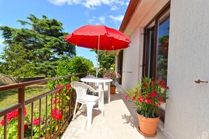 A balcony with a table and chairs, a red umbrella, and potted plants. - Apartment 1674 (Pula)